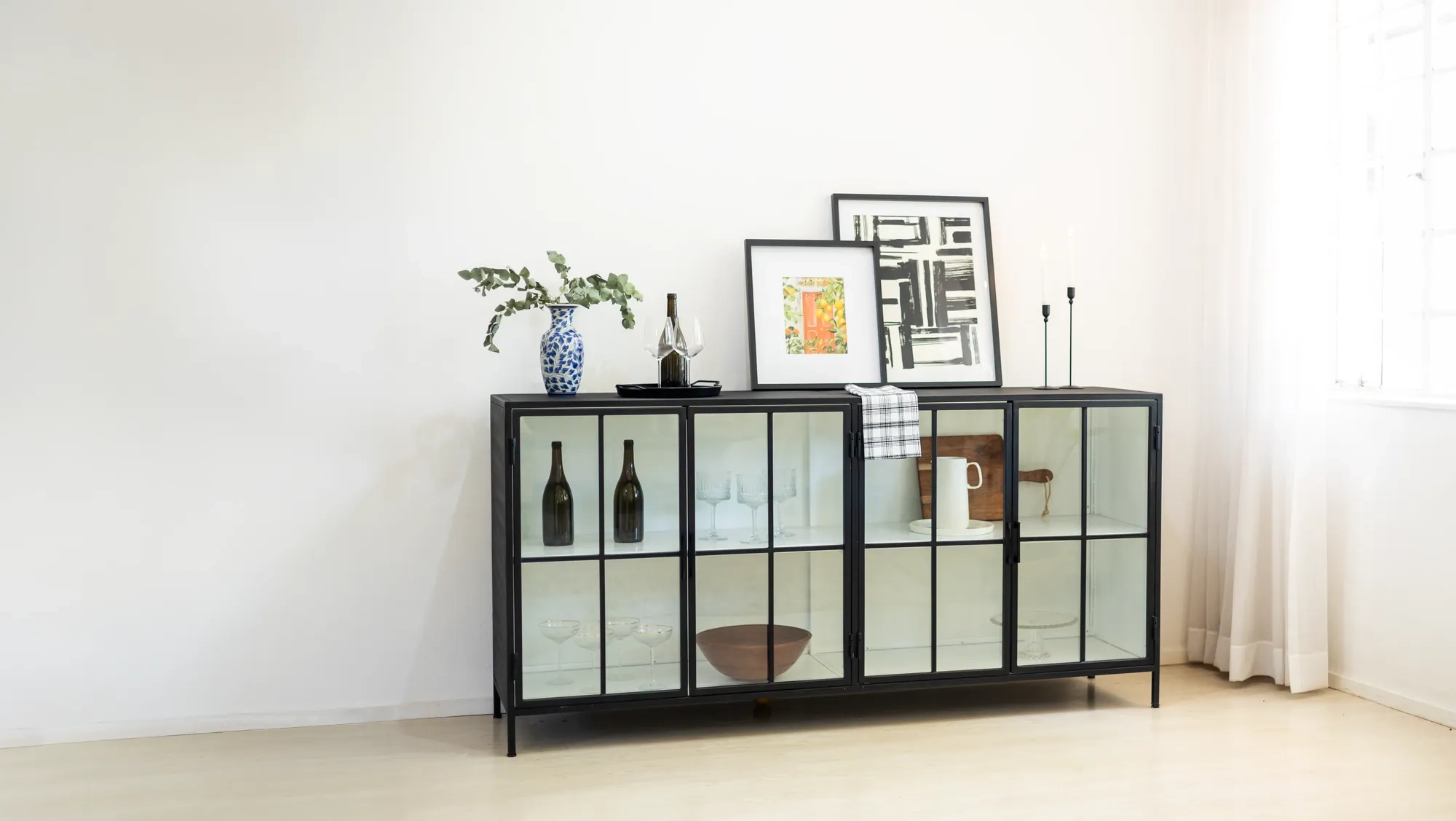 Black steel and glass four-door sideboard styled with glassware and framed art